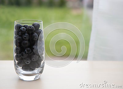 Sweet tasty bilberries in pot. fresh blueberries with a glass goblet. Blueberries in a glass on the windowsill. White curtain in Stock Photo