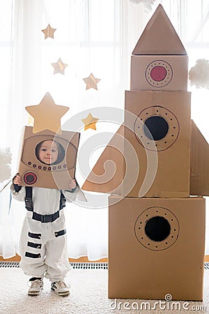 Sweet toddler boy, dressed as an astronaut, playing at home with cardboard rocket and handmade helmet Stock Photo