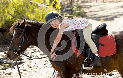 Sweet young girl hugging pony horse smiling happy wearing safety jockey helmet in summer holiday Stock Photo