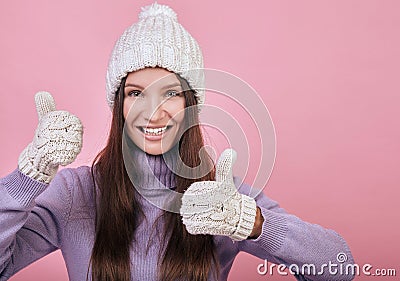 Sweetly pretty girl in a knitted hat, purple sweater and mittens shows super sign or like Stock Photo
