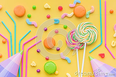 Sweets for birthday including lollipop, macarons and drops on yellow background top view Stock Photo