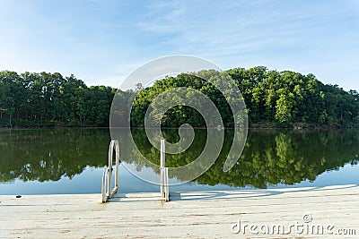 A swim ladder on a dock on Lake Lanier in Georgia with a reflection of green trees in the water Stock Photo