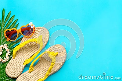 Swimming accessories - sunblock, heart - shaped glasses, yellow flip flop, palm, shells bracelet isolated on blue background Flat Stock Photo