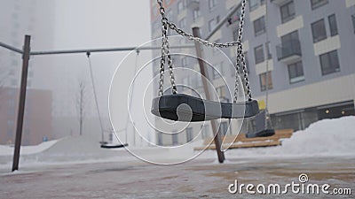 Swing on background of houses in fog. Action. Empty swing eerily seesaw on background of fog. Empty playground in cloudy Stock Photo