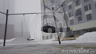 Swing on background of houses in fog. Action. Empty swing eerily seesaw on background of fog. Empty playground in cloudy Stock Photo