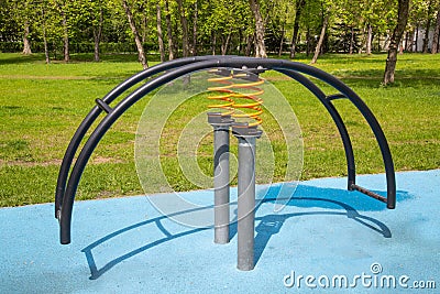 Swing on a yellow metal spring in the form of a curved arc on a playground with a rubberized surface. Kids sports Stock Photo