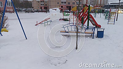 Swings, slides and benches are installed on the playground among residential buildings. A snowman made of snow by children is also Stock Photo