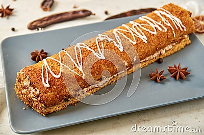 Swiss roll with sweet white cream on gray plate decorated with white cloth, star anise and ripe carob fruit pods Stock Photo