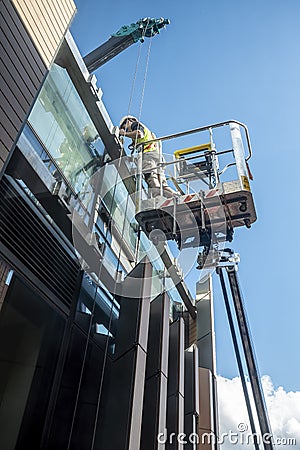 Workman hoisted using a mechanical crane to a high level Editorial Stock Photo