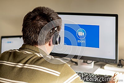 Man with headphones looking on the monitor with zoom cloud meetings logo Editorial Stock Photo