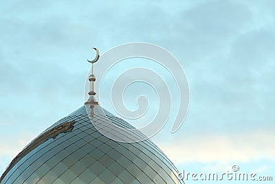 The symbol of Islam is a golden crescent moon on top of the mosque minaret on the blue morning sky with clouds. Stock Photo