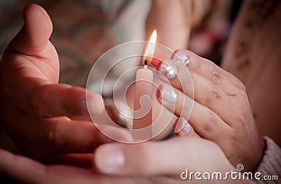 Four hands of young people protecting fragile candle light fire as a metaphor of care and protection during religious ceremony Stock Photo