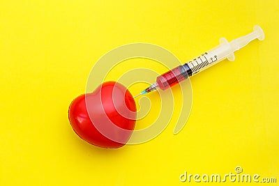 Syringe give medicine to red heart shape on yellow background. U Stock Photo