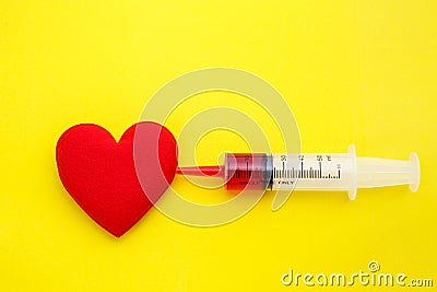 Syringe give medicine to red heart shape on yellow background. U Stock Photo