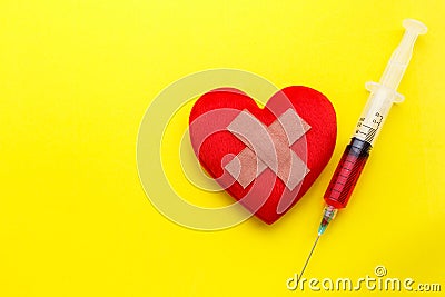 Syringe give medicine to red heart shape on yellow background. U Stock Photo