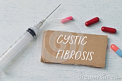 Syringe injection, pill capsules and brown card with text CYSTIC FIBROSIS Stock Photo