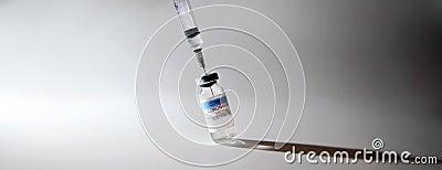 The syringe is stuck in the cap of a glass tilted bottle with a transparent covid vaccine Stock Photo