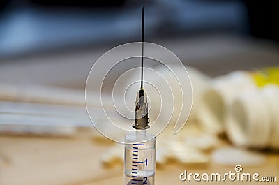 A syringe with a needle on the background of medicines and a wooden table Stock Photo