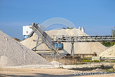 A system of interconnected conveyor belts over heaps of gravel against a blue sky at an industrial cement plant. Stock Photo