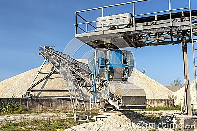 A system of interconnected conveyor belts over heaps of gravel against a blue sky at an industrial cement plant. Stock Photo