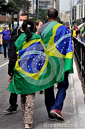 Couple holding hands and the Brazilian flag on their back walking along Paulista avenue Editorial Stock Photo