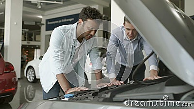 Säljaren visar motorn av den moderna automatiskn till en köpare i bilvisningslokal arkivfilmer Säljaren visar motorn av den moderna automatiskn till en köpare i bilvisningslokal arkivfilmer