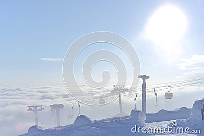T-bar and gondola lifts emerge through and above the clouds. Photo into the bright sun Stock Photo