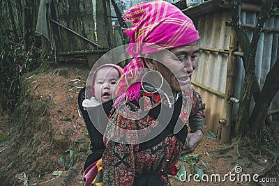A small child in a bag behind a teenage girl. Red dzao - a small nation of North Vietnam Editorial Stock Photo