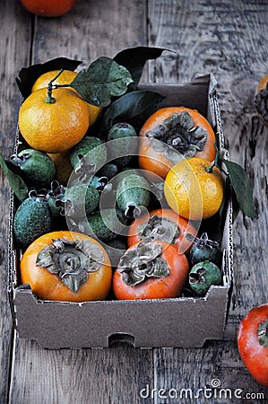 On the table in a box a fresh persimmon, feijoa and citrus mandarins Stock Photo
