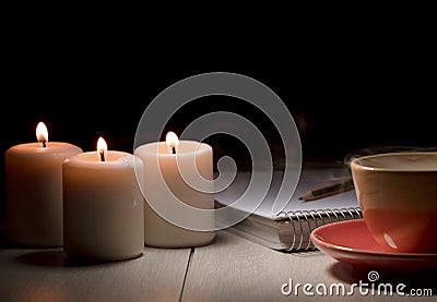 table with burning candles notebook pencil books, yellow mug with steam smoke Stock Photo