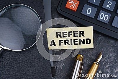 On the table is a calculator, a pen and a notebook with a bookmark on which it is written - REFER A FRIEND Stock Photo