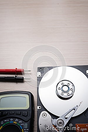 On the table lies an opened old hard drive and a multimeter for checking and repairing it Stock Photo