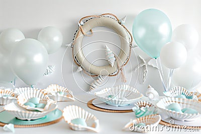 table with life ring wall decor, white and light blue balloons, and shellshaped dishes Stock Photo