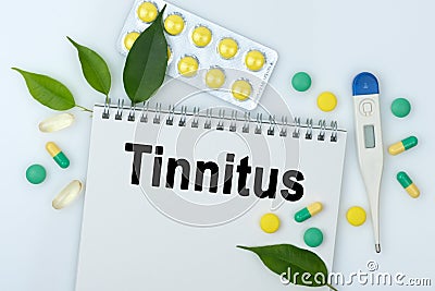 On the table are pills, a thermometer, leaves and a notebook with the inscription -Tinnitus Stock Photo