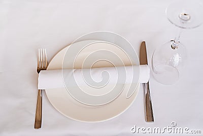 Table setting. empty white plate, towel, Cutlery, and upturned wine glass. Stock Photo