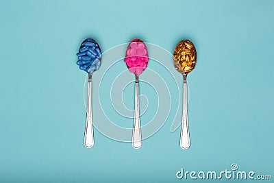 Table spoons filled with assortment of various colourful pills on blue pastel coloured background. Medication. Stock Photo