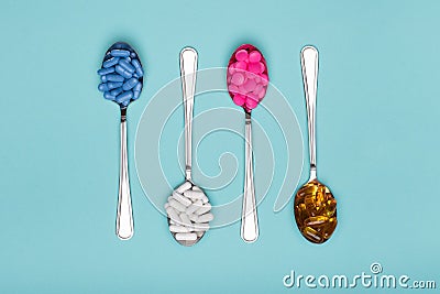 Table spoons filled with assortment of various colourful pills isolated on blue pastel coloured background. Antiobesity medication Stock Photo