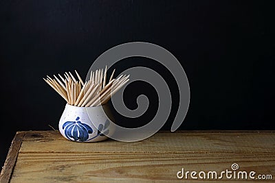 TABLE TOP IMAGE OF SHARP WOODEN TOOTHPICKS IN A CERAMIC CONTAINER ON A WOODEN BOARD Stock Photo