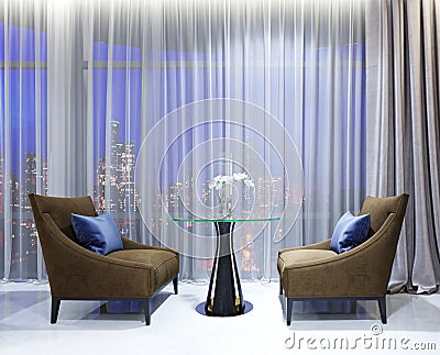 A table with two easy chairs in the contemporary lounge restaurant. Lighted comfortable space with large windows with evening Stock Photo