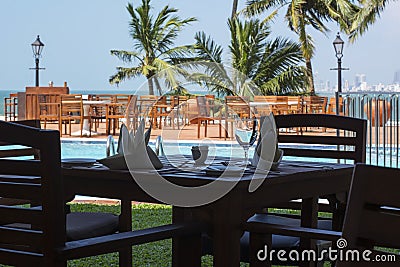 A table for two people near a swimming pool with green palm trees Stock Photo