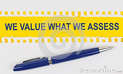 On the table are two sheets from a notebook and a pen on a yellow background written - WE VALUE WHAT WE ASSESS Stock Photo