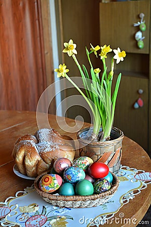 A table with a weave basket with multicolored dyed eggs, a pot with spring flowers and a sweet Easter bread Stock Photo
