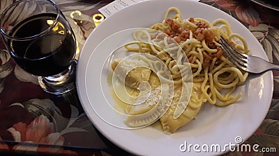 On the table, a white plate with Italian pasta and a glass of wine in the city of Gramado Editorial Stock Photo