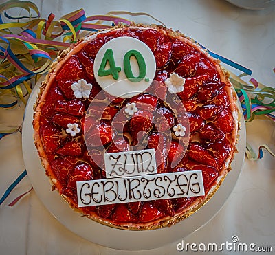 Table with a white tablecloth there is a red birthday strawberry cake with the inscription Stock Photo