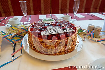 Table with a white tablecloth there is a red birthday strawberry cake with the inscription Stock Photo