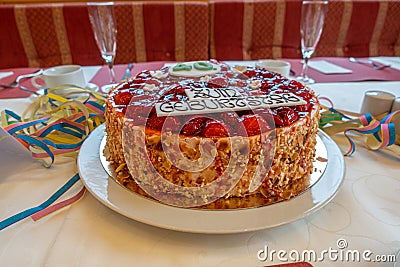 Table with a white tablecloth there is a red birthday strawberry cake with the inscription Stock Photo