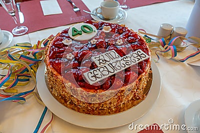 Table with a white tablecloth there is a red birthday strawberry cake with the inscription Stock Photo