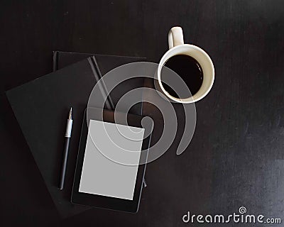 Tablet with blank screen on top of stacked books and a pen with a cup of coffee on a black background. Stock Photo