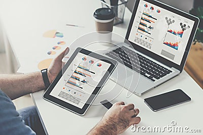 Tablet computer with graphs,diagrams and charts on screen in hands of young bearded businessman sitting at table Stock Photo