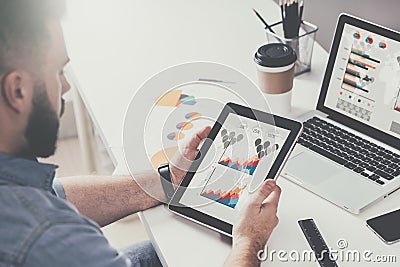 Tablet computer with graphs, diagrams and charts on screen in hands of young bearded businessman sitting at table Stock Photo